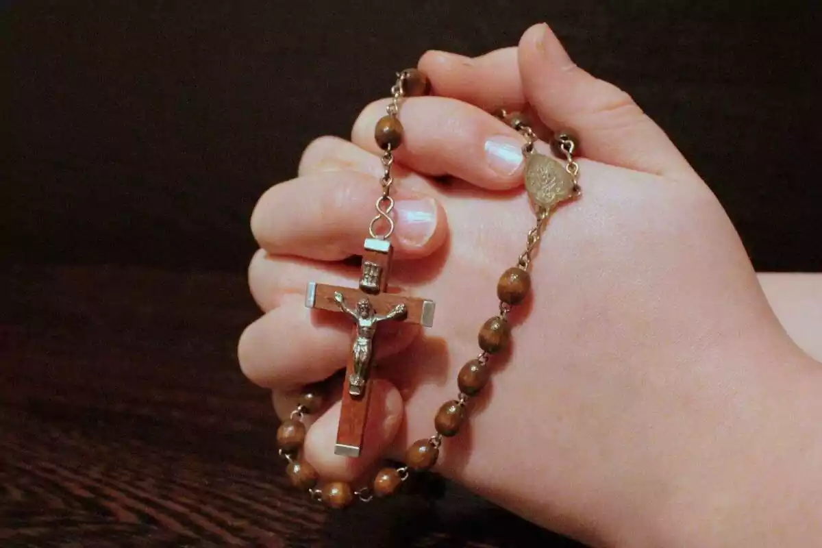 Persona sosteniendo un rosario con una cruz, entre las manos