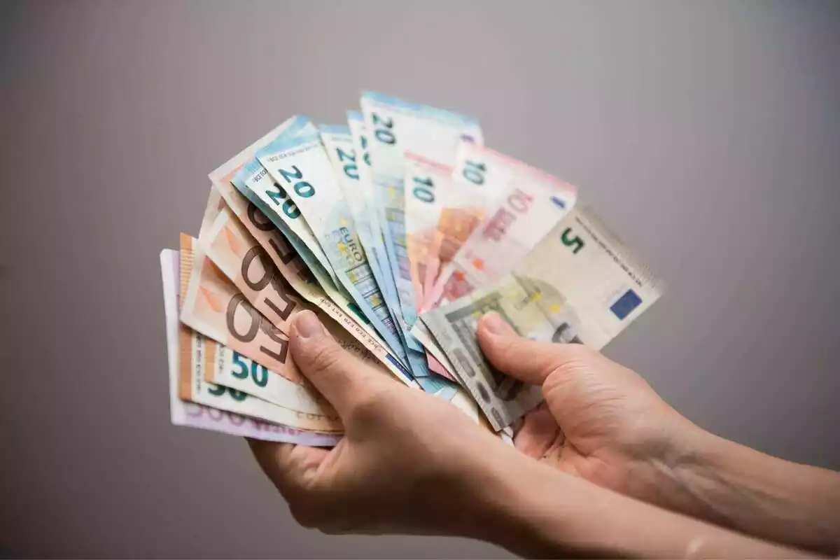 Dos manos de una persona mostrando diferentes tipos de billete de euro en forma de abanico