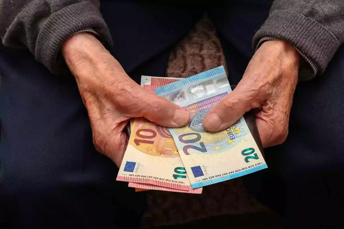 Las manos de una persona mayor cogiendo varios billetes de euro