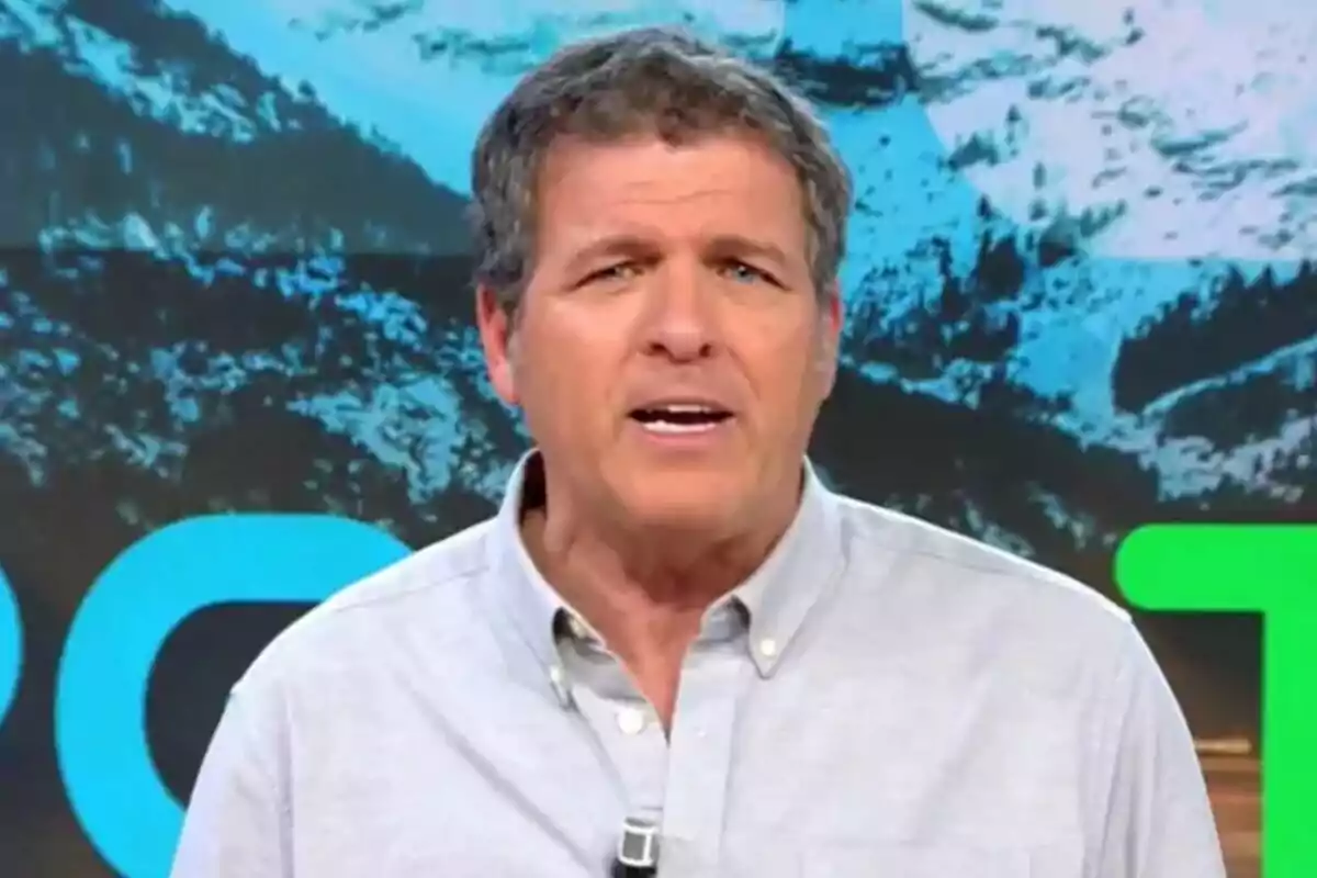 Mario Picazo con una camisa gris claro está hablando frente a un fondo con un paisaje montañoso.