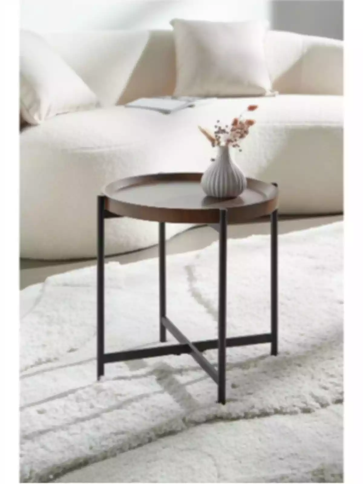 Round wooden side table with black metal legs, decorated with a small vase, in front of a white sofa on a light-colored rug Round wooden side table with black metal legs, decorated with a small vase, in front of a white sofa on a light-colored rug