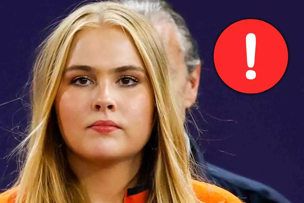 Amalia de Holanda con expresión seria y un círculo rojo con un signo de exclamación blanco al fondo Amalia de Holanda con expresión seria y un círculo rojo con un signo de exclamación blanco al fondo