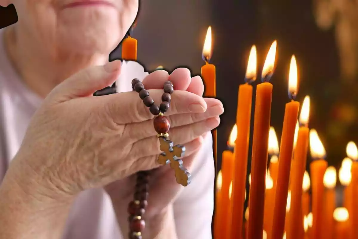 Mujer rezando con un rosario en las manos y unas velas de iglesia en el fondo