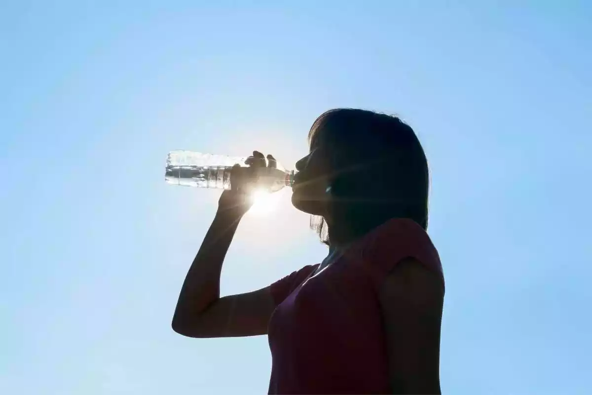 Mujer con camiseta rosa bebiendo agua debajo del sol