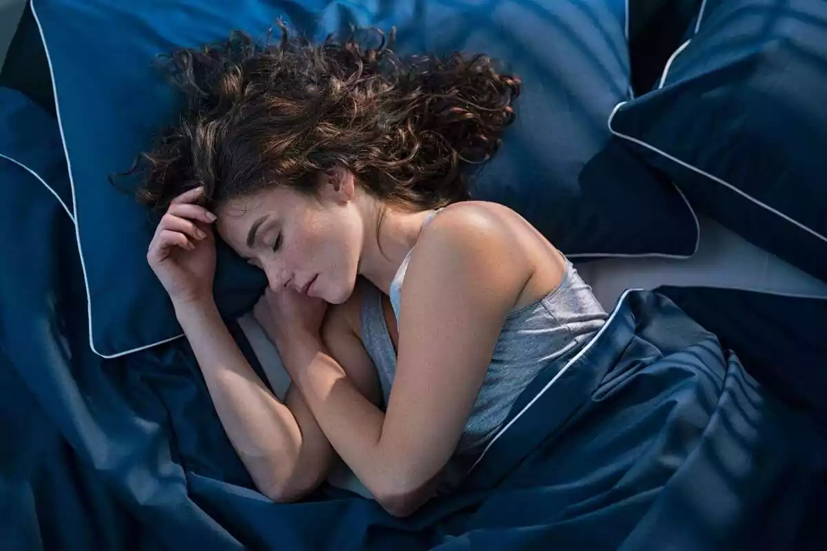 Mujer durmiendo en una cama con sábanas de color azul marino