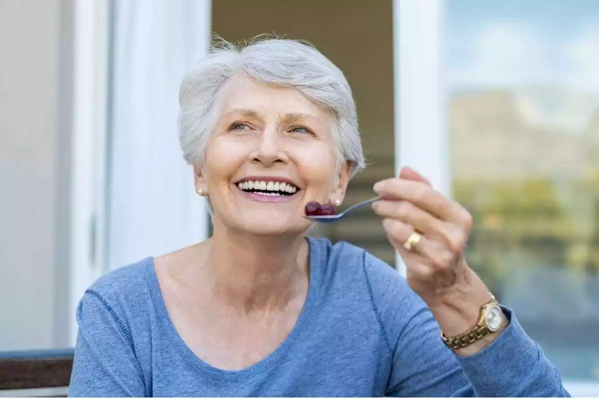 Mujer mayor sonriendo con una cuchara con fruta en la mano