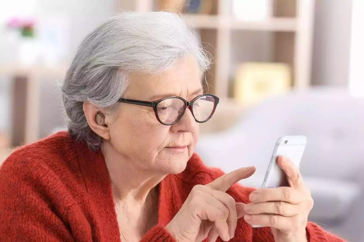 Una mujer mayor escribiendo en su teléfono móvil con las gafas puestas