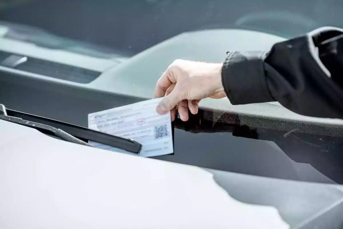 Una persona poniendo una multa en un coche