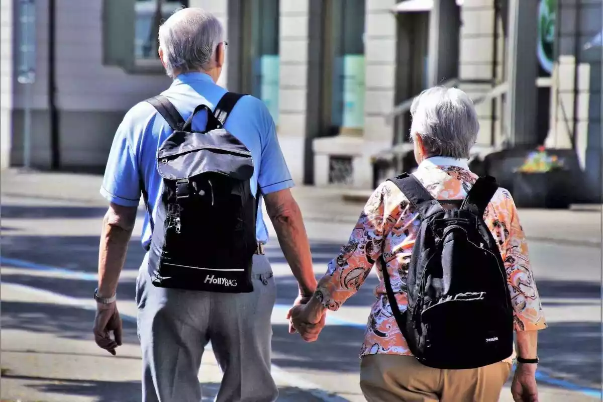 Un hombre y una mujer mayores caminando por la calle con mochilas
