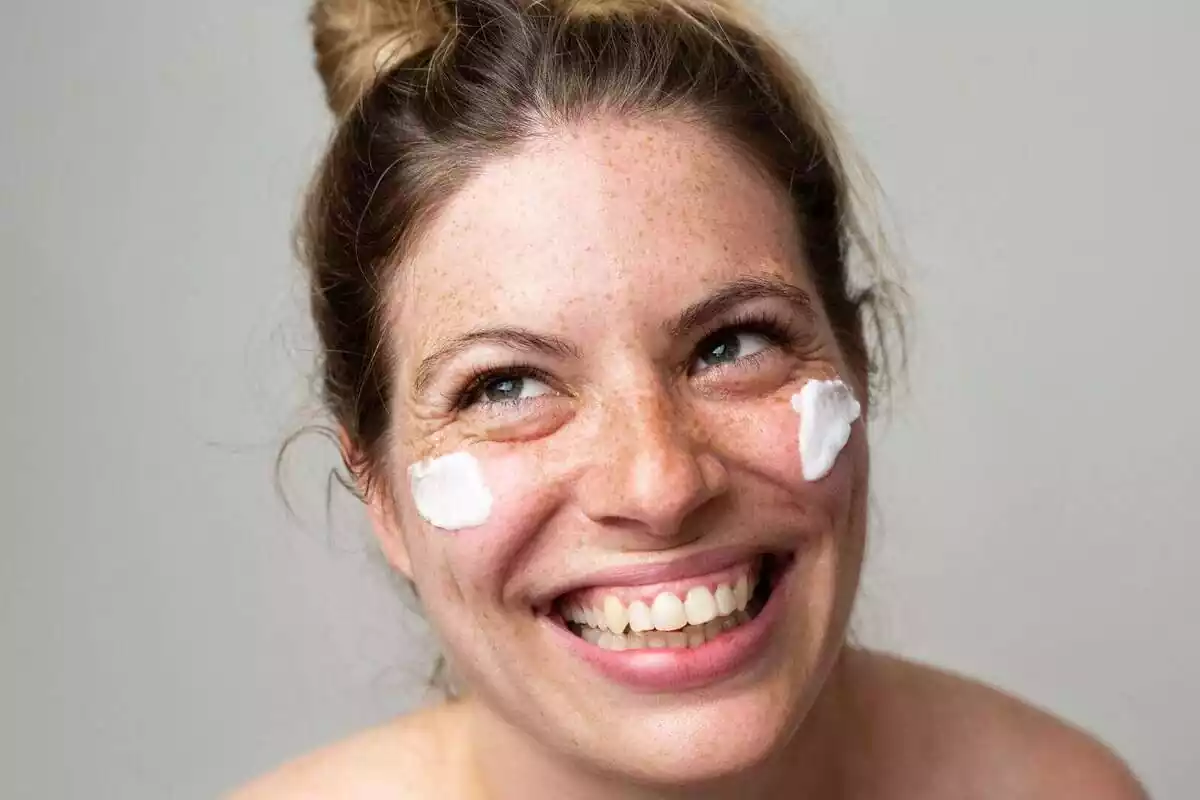 Mujer sonriente con pecas y crema solar en el rostro