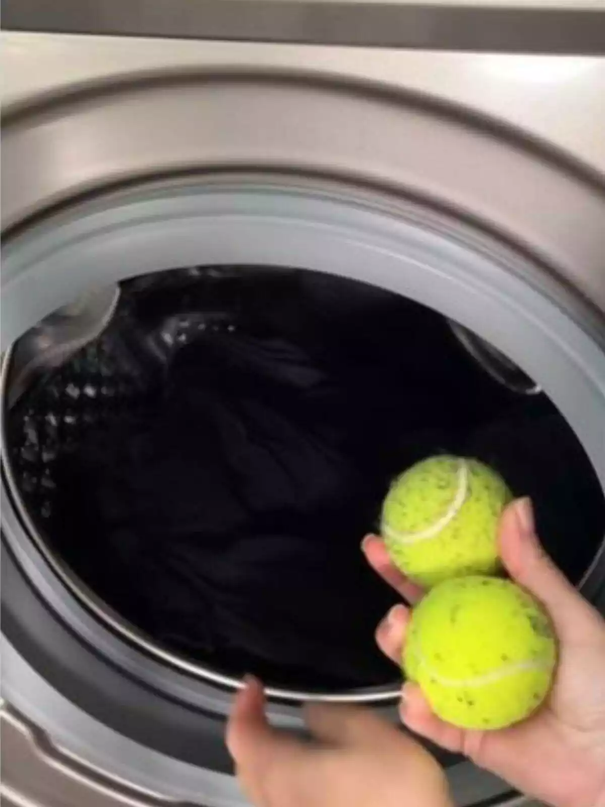 Imagen de una persona con pelotas de tenis en la mano a punto de meterlas en una lavadora