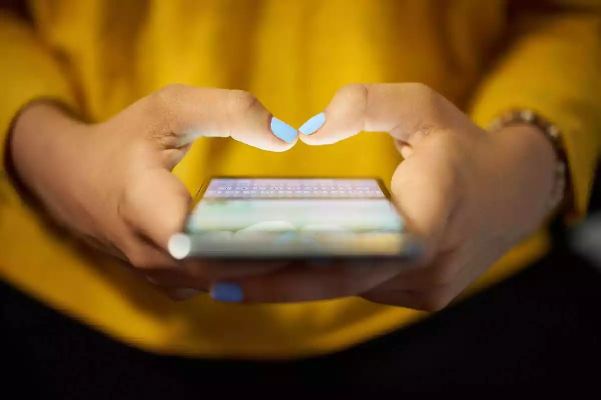 Manos de una persona con las uñas pintadas de azul, escribiendo en un móvil