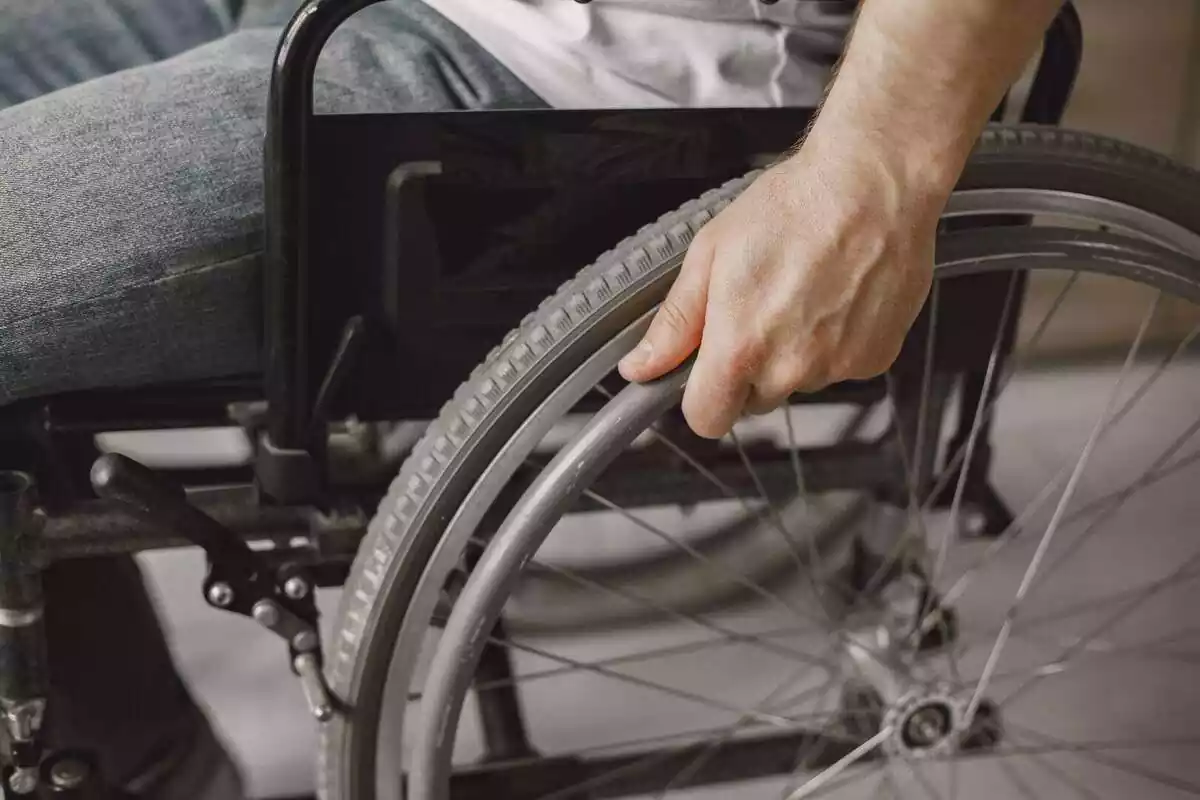 Una persona en silla de ruedas con la mano tocando una rueda