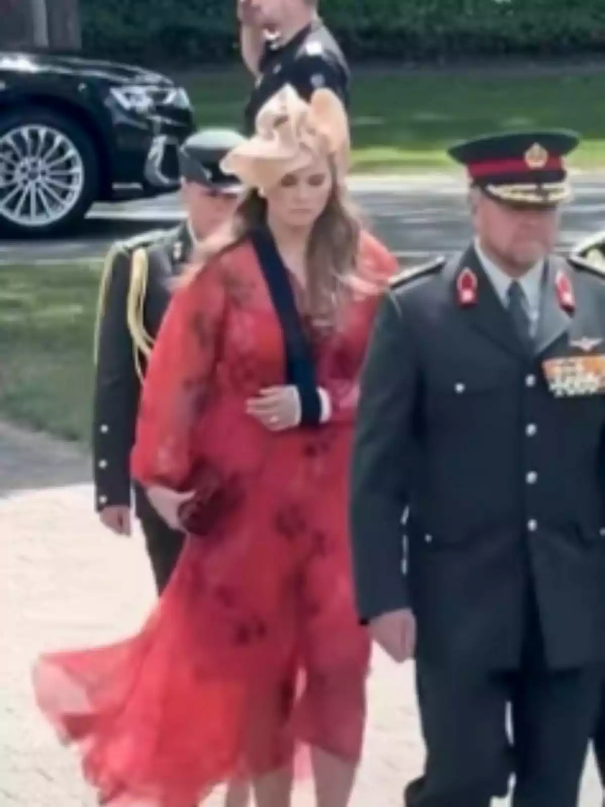La princesa Amalia de Holanda vestida con un vestido rojo y sombrero elegante camina junto a hombres con uniforme militar en un evento al aire libre. La princesa Amalia de Holanda vestida con un vestido rojo y sombrero elegante camina junto a hombres con uniforme militar en un evento al aire libre.