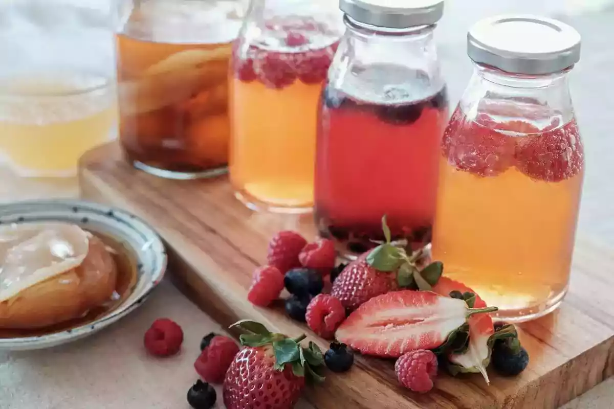 Frascos de vidrio con bebidas de colores y frutas como fresas, frambuesas y arándanos sobre una tabla de madera. Frascos de vidrio con bebidas de colores y frutas como fresas, frambuesas y arándanos sobre una tabla de madera.