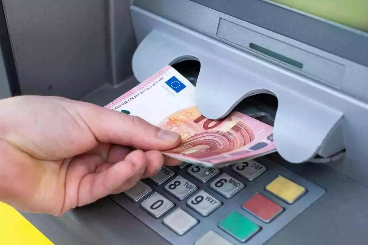 Mano izquierda de una persona sacando billetes en un cajero automático