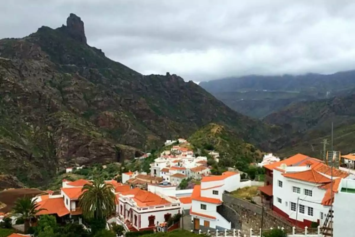 Vista panorámica de un pequeño pueblo con casas de techos rojos rodeado de montañas y vegetación bajo un cielo nublado.