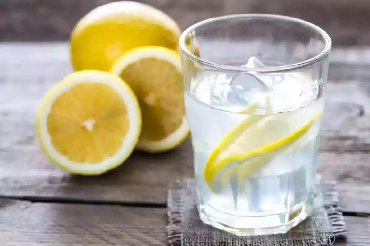 Un vaso de agua con rodajas de limón y hielo sobre una mesa de madera junto a limones frescos. Un vaso de agua con rodajas de limón y hielo sobre una mesa de madera junto a limones frescos.