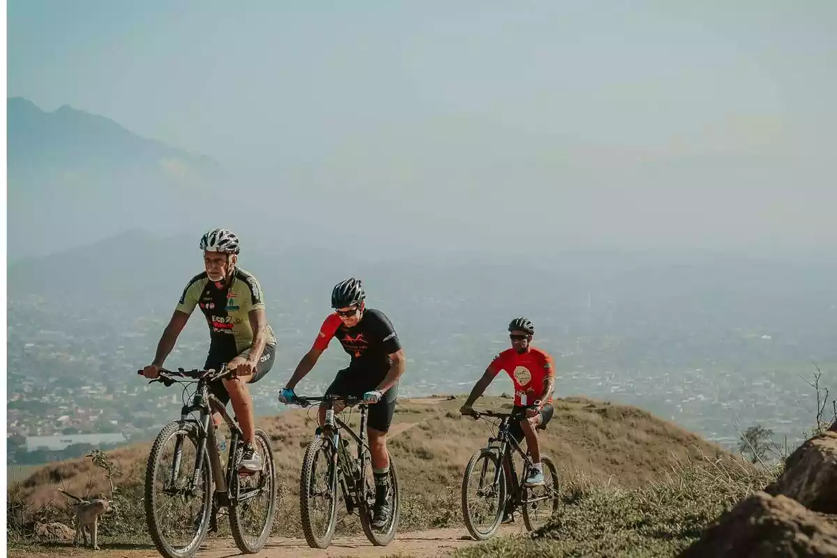 Tres personas con traje de ciclista y casco montando en bici por la montaña