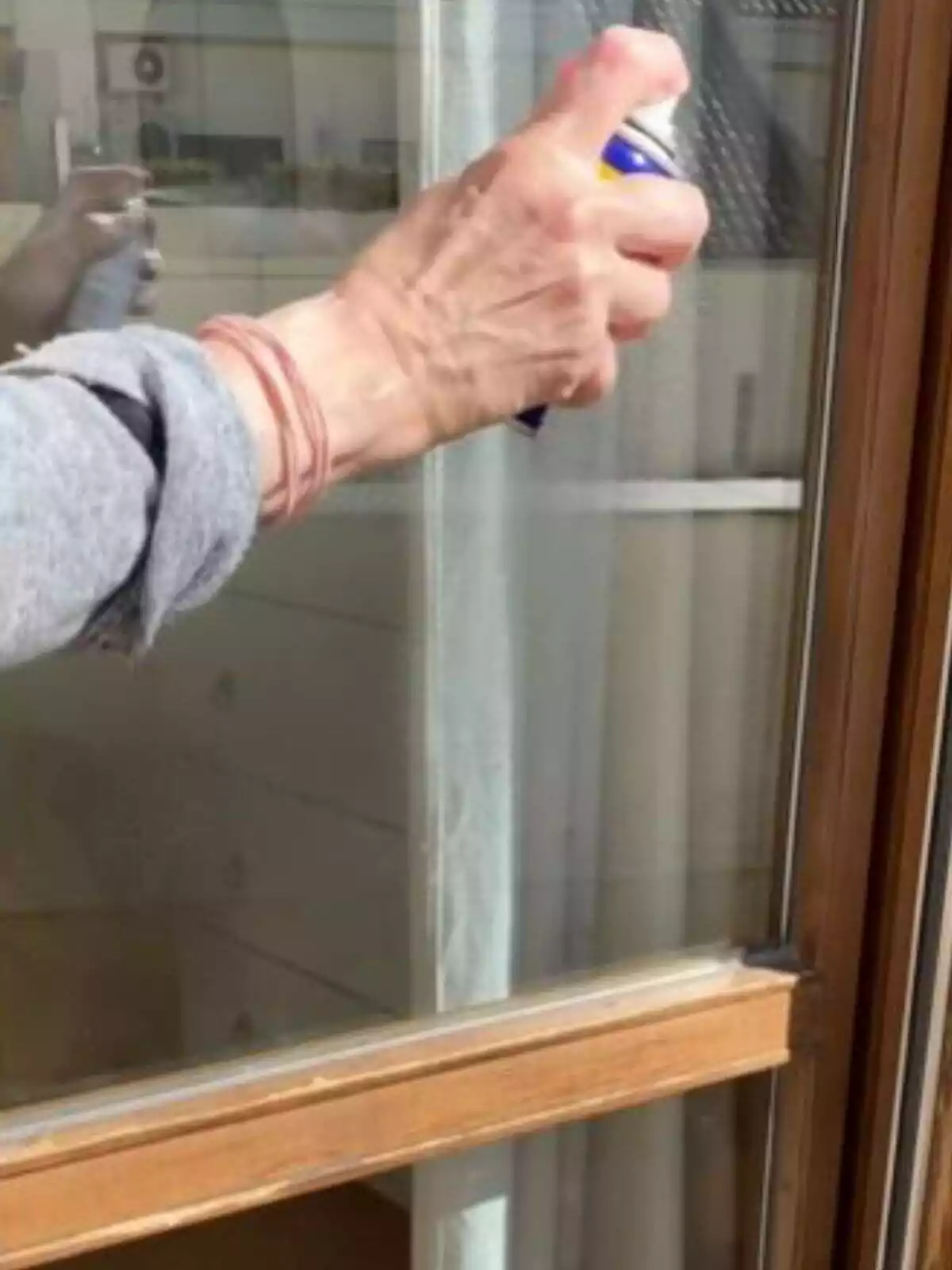 Imagen de una persona con un 3 en 1 en la mano, rociando una ventana