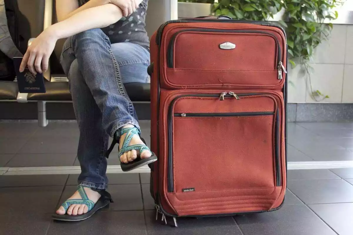 Una persona sentada esperando con una maleta al lado