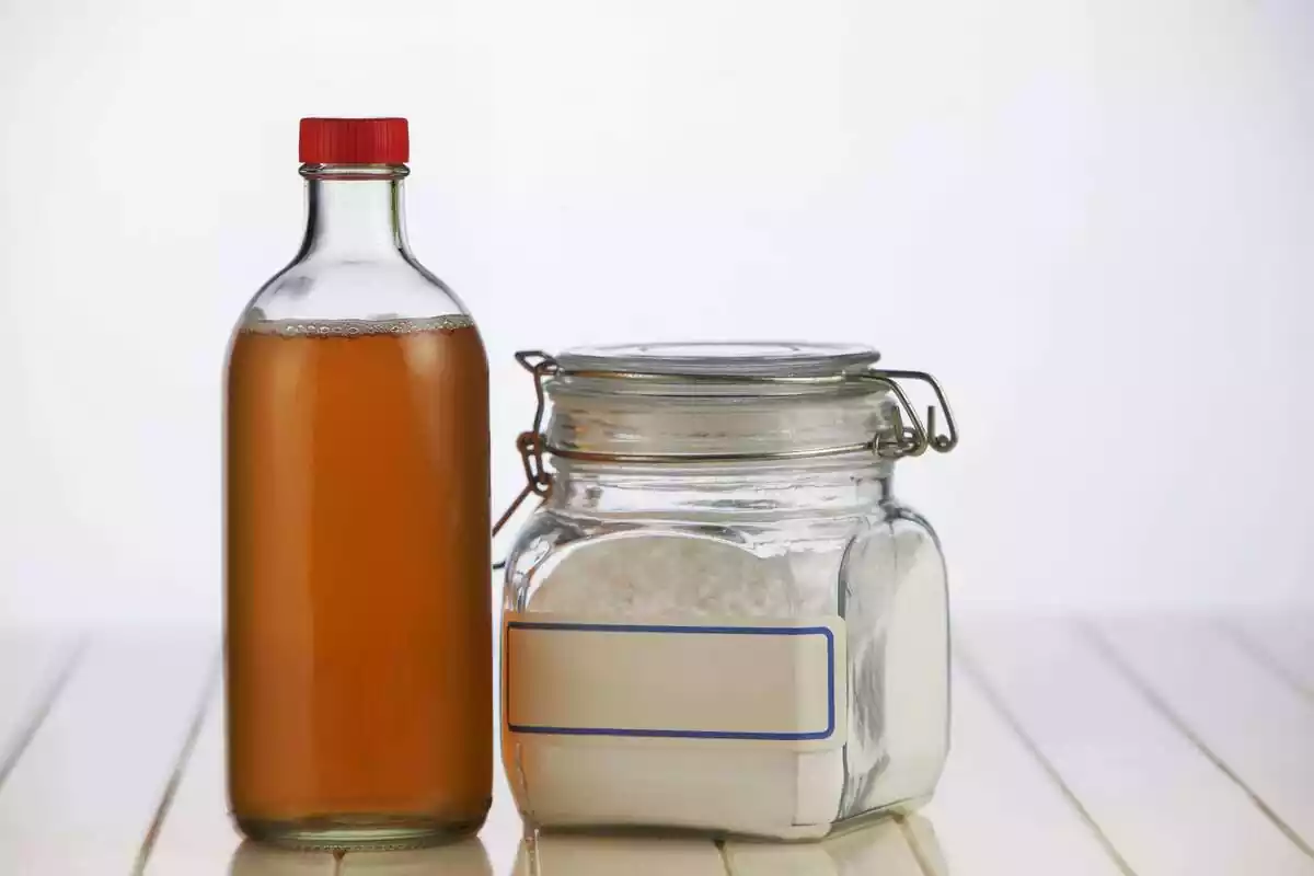 Una botella de vinagre al lado de un recipiente con bicarbonato