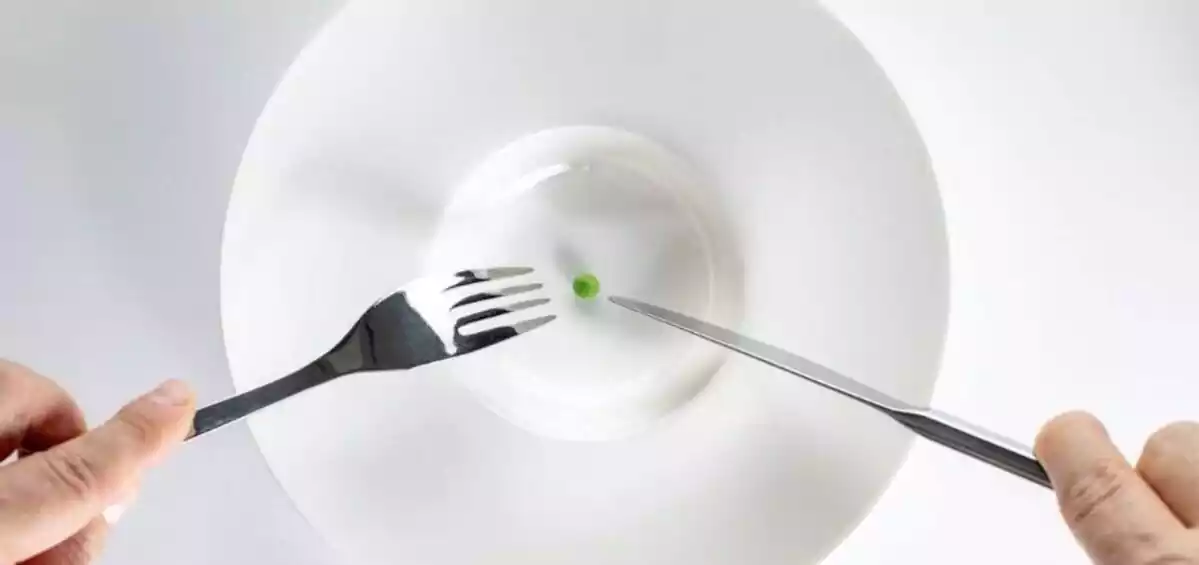 Un plato blanco con un guisante y cuchillo y tenedor en mano